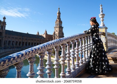 Spanish, Beautiful, Brunette Flamenco Dancer With A Typical Flamenco Dress In Black With White Polka Dots. She Is In The Plaza Spain In Seville. Flamenco Concept Cultural Heritage Of Humanity.