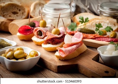 Spanish cuisine. Tapas with sliced sausage, bacon, salami, olives, dried tomatoes and parsley on a wooden table.