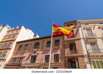 Spanish flag in the old town of the city of Malaga. Beautiful typically Spanish buildings architecture in background. Blue sky in a sunny summer day