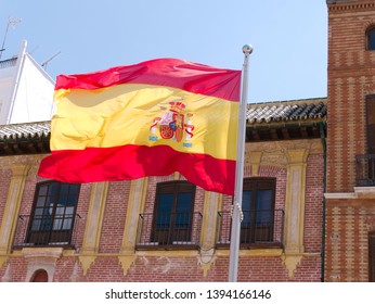 Spanish Flag Waving In Front Of An Old Red Brick Building In The City Of Malaga, Spain.