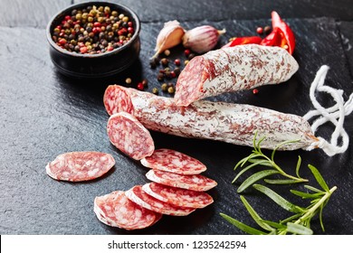 Spanish Fuet Sausages Cut In Slices On A Black Slate Plate With Peppercorns, Sliced Chili And Fresh Rosemary, View From Above, Close-up