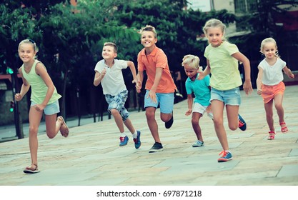 Spanish  Kids Actively Playing And Running Together On Street On Summer Day
