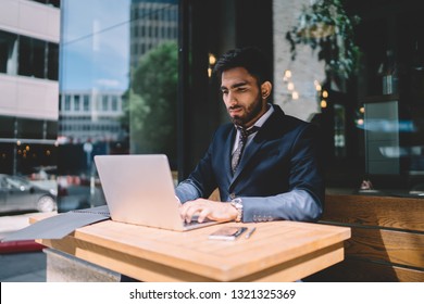 Spanish Male Economist Working With Report Via Program On Laptop Computer Connected To Cafeteria Wifi, Handsome Business Man In Formal Wear Keyboarding Text For Document During Messaging With Director