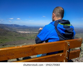 A Spanish Man Mountaineer Sitting On A Wooden Bench On The Top Of The Mountain