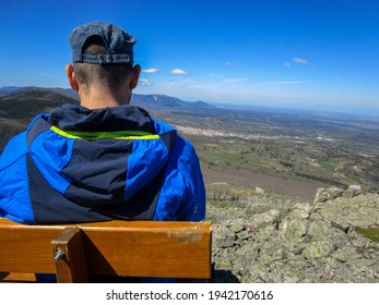 A Spanish Man Mountaineer Sitting On A Wooden Bench On The Top Of The Mountain,