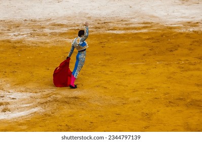 A Spanish matador in a beautiful smart suit with a muleta in his hand in the arena. A brave angry bullfighter preparing to meet the bull Toro bravo. The bullfighter greets the crowd of spectators  