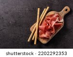 Spanish serrano ham with olives and breadstick on black background. Top view. Copy space