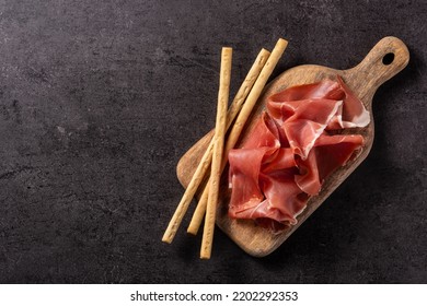 Spanish serrano ham with olives and breadstick on black background. Top view. Copy space