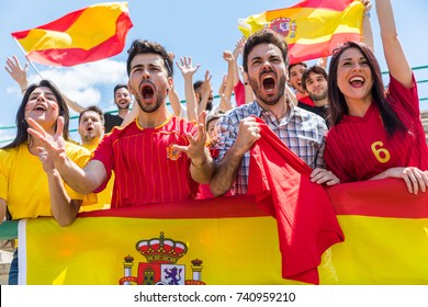 Spanish supporters cheering at stadium with flags. Group of fans watching a match and cheering team Spain. Sport and lifestyle concepts.