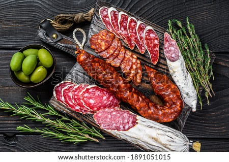 Spanish tapas sliced sausages salami, fuet and chorizo on a wooden cutting board. Black wooden background. Top view.