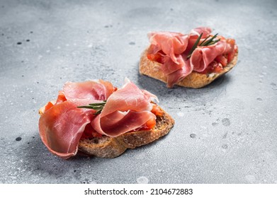 Spanish Tapas with tomatoes and cured Slices of jamon iberico ham, fresh toasts. Gray background. Top view