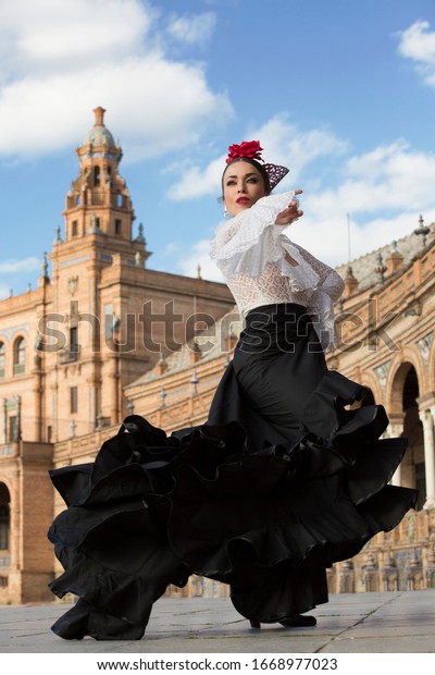 Spanish woman dancing flamenco dance in\
a beautiful monumental place. She is wearing a traditional black\
dress, a white shirt, a red flower and a\
headpiece.