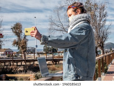 A Spanish Woman In A Face Mask Taking A Selfie With Her Laptop On Fence In The Park