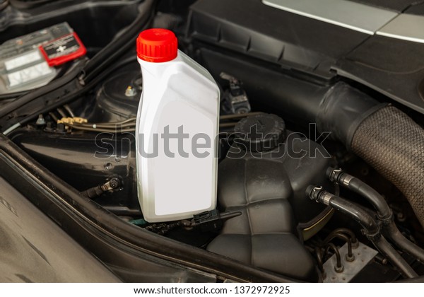 Spare part for car engine one liter bottle or\
can of lubricant in gray with red cap on a background with under\
hood compartment. Maintenance and oil change in auto service\
industry.
