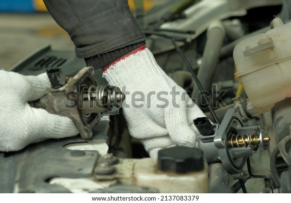 Spare parts for the car. An auto mechanic\
replaces a faulty car thermostat during car maintenance at a\
service center.