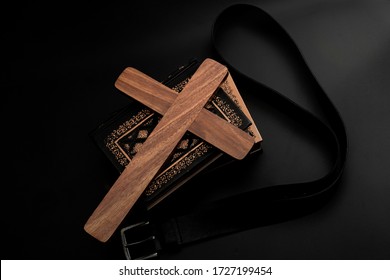 Spare The Rod, Spoil The Child, Lost Innocence And Children Abuse Concept With Religious Wood Cross, Stack Of Books And Leather Belt Isolated On Dark Black Background