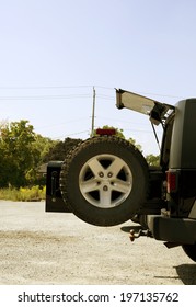 A Spare Tire Is Mounted On The Back Door Of A Vehicle Parked On A Road.