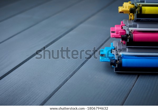 Spare toner cartridges for\
cyan, magenta and yellow color laser printer on gray wooden\
background