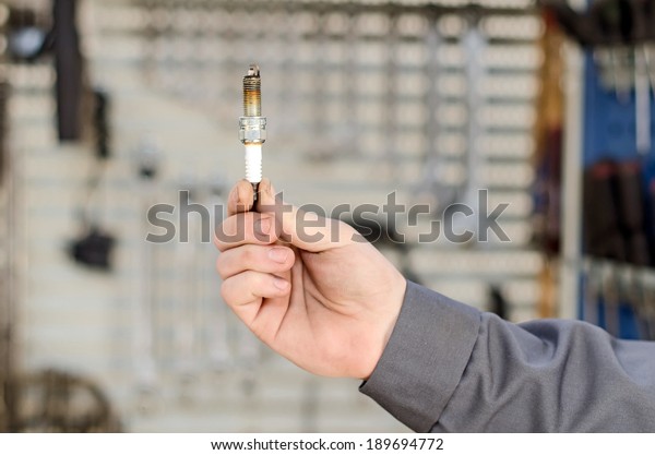 Spark plug\
in hand against the cabinet with\
tools.