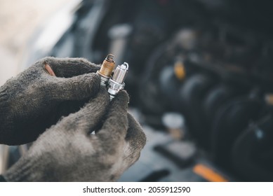 Spark plug replacement work, Hand of the auto mechanic holding the old spark plug on blurred engine car on background. - Shutterstock ID 2055912590