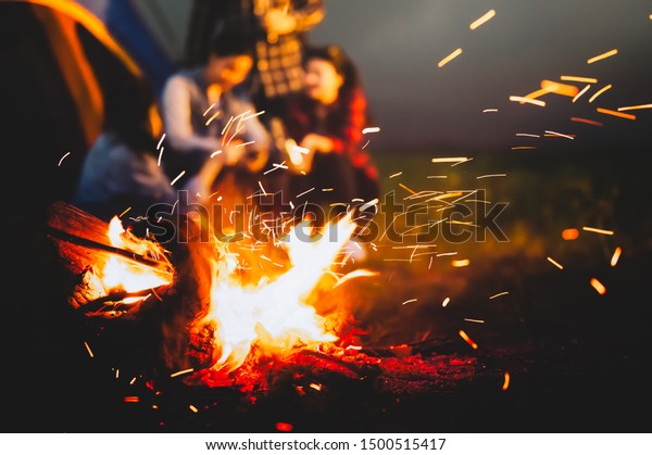 Sparking bonfire with tourist people sit around\
bright bonfire near camping tent in forest in summer night\
background. Group of student at outdoor fire fuel. Travel  activity\
and long vacation\
weekend