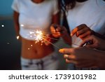 The sparklers in the hands of young girls on the beach. Three girls enjoying party on beach with sparklers. Summer holidays, vacation, relax and lifestyle concept.