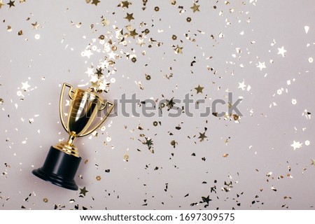 Sparkles grey background with a winners cup. Flat lay style.