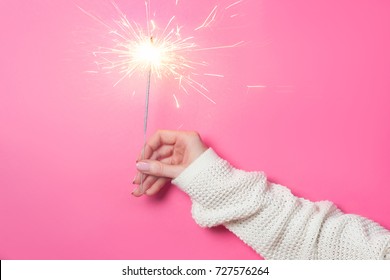 Sparkling Bengal fire in a woman's hand on a pink background. Christmas Holiday Concept