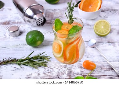 Sparkling beverage with slices of lime, kumquat and orange topped with mint against the white wooden background