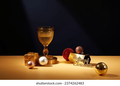 Sparkling Christmas ornaments displayed surrounded a yellow wine glass over dark background. Christmas is also often used to refer to the entire Christmas season