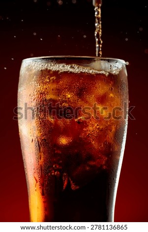 Sparkling cola is poured into a misted glass with ice cubes.