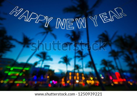 Sparkling Happy New Year message hanging in silver bunting over brightly colored tropical background of the Miami skyline in defocus
