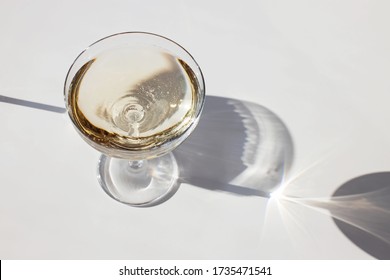 Sparkling Wine In A Glass On The White Table In Natural Sunlight With Shadows. Minimalist Creative Composition