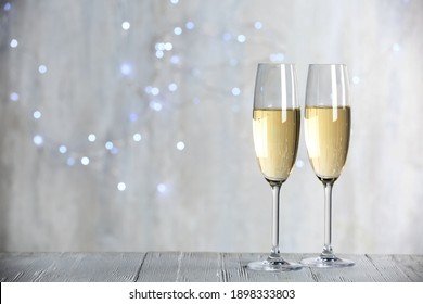 Sparkling wine in glasses on wooden table against blurred lights, space for text