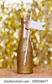 Sparkly Mini Champagne Bottle With Tags On Bright Sparkling Blurred Background 