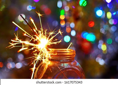 Sparks from burning Sparkler candle in glass jar on wooden table on blurred background with glowing garland close up - Powered by Shutterstock