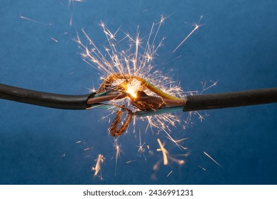 Sparks explosion between electrical cables, on blue background, fire hazard concept, soft focus close up