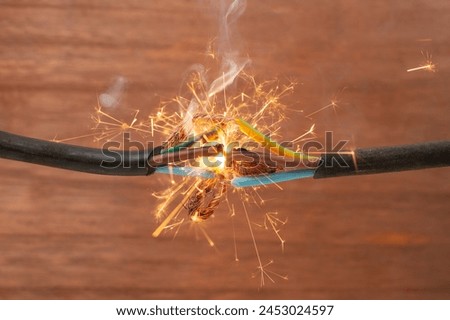 Sparks explosion between electrical cables, on brown wooden background, fire hazard concept, soft focus close up
