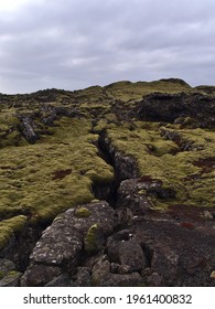 Sparse landscape with deep rocky fissure on lava field with volcanic rocks covered by green moss and lichens near Grindavik, Reykjanes peninsula, Iceland on cloudy day in winter season.