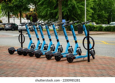 Spartanburg, SC, USA - September 16, 2021: Eight Blue Duck E-scooters Are Lined Up On A Red Brick Sidewalk In An Urban Downtown.