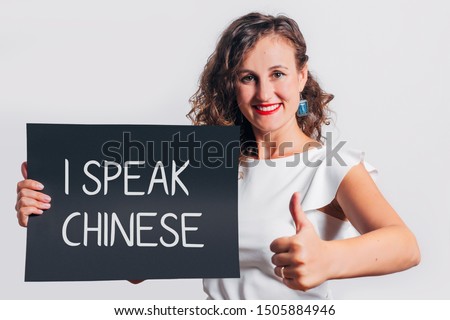 I speak Chinese phrase inscription on a board held by a smiling gesturing woman.