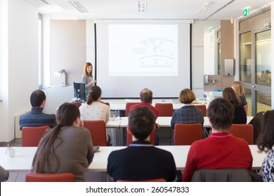 Speaker giving presentation in lecture hall at university. Participants listening to lecture and making notes. Copy space for brand on white screen.
