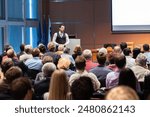 Speaker giving a talk in conference hall at business meeting event. Rear view of unrecognizable people in audience at the conference hall. Business and entrepreneurship concept.