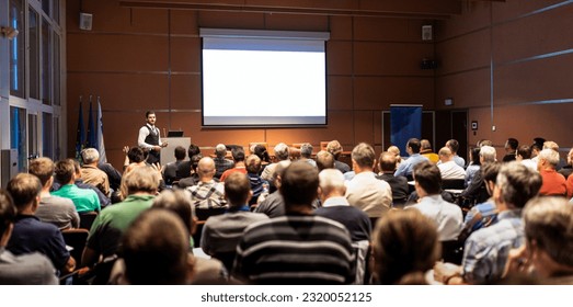 Speaker giving a talk in conference hall at business meeting event. Rear view of unrecognizable people in audience at the conference hall. Business and entrepreneurship concept. - Powered by Shutterstock