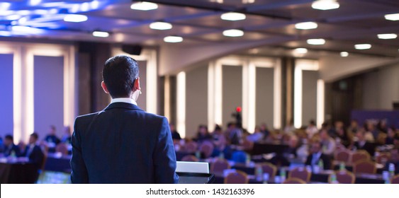 Speaker giving a talk at a corporate business conference.
Audience in hall with presenter in front of presentation screen. Corporate executive giving speech during business and entrepreneur seminar. - Powered by Shutterstock