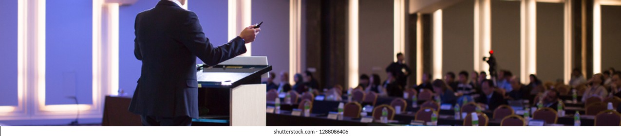 Speaker At Talk In Business Conference. Corporate Speaker On Stage At Seminar. Presenter Giving Business Presentation At Meeting. Corporate Exhibition For Investors Event.
