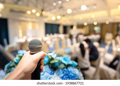 A Speaker's Hand Is Holding Wireless Microphone, Prepare For Speaking In The Education Seminar Or Business Townhall Conference On The Stage. Close-up And Mic And Hall Room As Blurred Background.