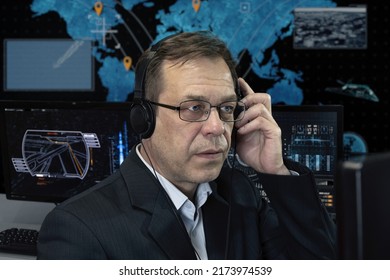 A Special Agent With Headphones Looks At The Monitor Against The Background Of The World Map. Concept: Missile Launch, Surveillance Of People, Military Analytical Center, Military Operations.