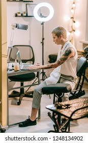 Special Armchair. Unusual Young Woman Sitting In Her Working Area With Laptop In Special Tattoo Studio