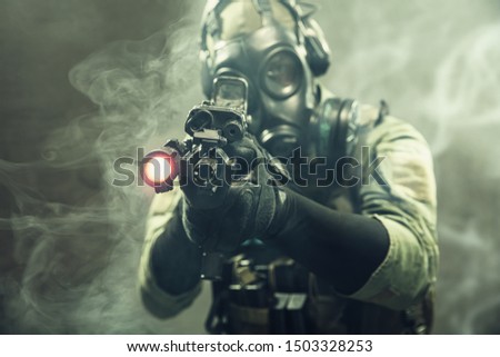 Special force soldier with gasmask between smoke at battlefield is aiming the target